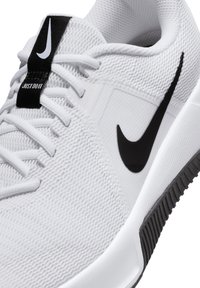 Bijela atletska cipela s teksturiranom mrežastom gornjom stranom, crnim Nike swoosh logotipom i oznakom "Just Do It". Gumeni potplat s vidljivim uzorkom.