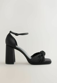 Sort blokhælset sandal med en knyttet forrem, plisseret tekstureret design og ankelrem med en lille spænde. Glat materiale finish.
