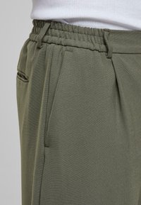Pantalons olive décontractés avec une taille élastique, des plis et des poches latérales. Fabriqués en tissu doux et texturé.