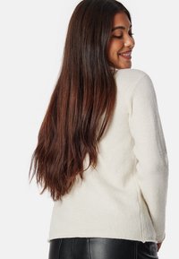 Witte, gestructureerde trui met lange mouwen en een relaxte fit, met een ronde hals en zijsplitten, gedragen met zwarte broek.
