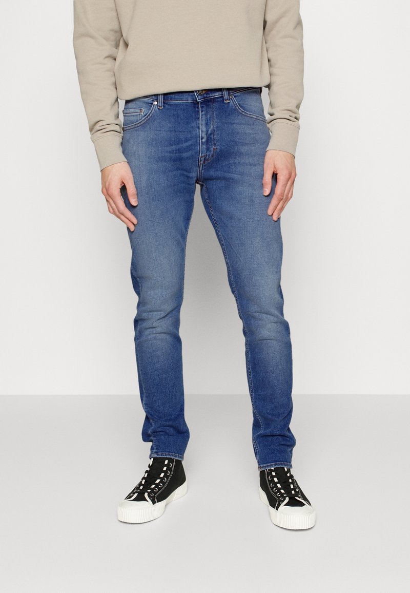 Blå slim-fit jeans i denim, med fem fickor och medium tvätt, tillsammans med svarta högtoppskor med vita gummisåler.