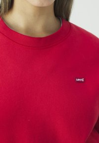 Gros plan sur une personne portant un sweat Levi's rouge, montrant l'encolure et le logo sur la poitrine.