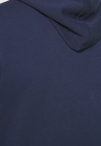 Felpa blu navy realizzata in un tessuto morbido, con una texture liscia e un cappuccio spazioso, arricchita da una sottile cucitura sul retro.