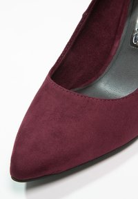 Escarpin en daim bordeaux à bout pointu avec une semelle intérieure noire lisse et un détail de couture minimal le long du bord. Design de talon solide pour la stabilité.