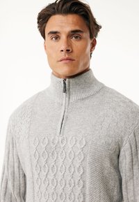 Grau gestrickter Pullover mit halbem Reißverschluss, der strukturierte Zopfmuster und gerippte Ärmel aufweist. Der Stoff hat eine weiche, geschichtete Optik.