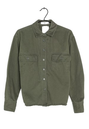 Chemise kaki boutonnée avec manches longues, deux poches avant à rabat boutonnées et un col, présentée sur un cintre noir.