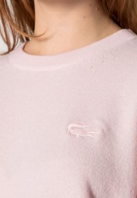 Jasnoróżowy bawełniany sweter z okrągłym dekoltem, z delikatnym, haftowanym logo na piersiach oraz miękką fakturą.