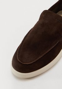 Brune semsket slip-on sko med en glatt, avrundet tå og beige gummisåle, med subtile sømdetaljer langs kantene.