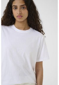 Biele bavlnené tričko s okrúhlym výstrihom, krátkymi rukávmi a voľným strihom. Tkanina pôsobí mäkko s hladkou textúrou. Žiadne viditeľné vzory.