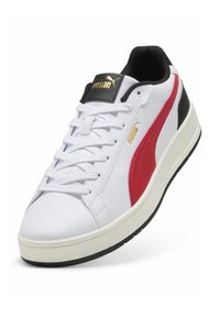 Baskets blanches avec une tige en cuir, des accents noirs, une bande rouge et une semelle épaisse blanche, avec des lacets et un logo doré sur la languette.