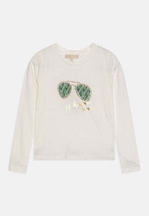 Chemise blanche à manches longues avec un motif de lunettes de soleil vertes à motifs et un texte doré manuscrit sur le devant.