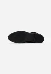 Semelle de chaussure noire avec une surface lisse, présentant un motif texturé et un design de vagues subtil pour l'adhérence. Matériau en caoutchouc robuste.