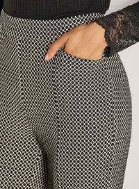 Hand met lichtbruine huid in de zak van zwart-wit gestippelde broek, draagt een zwart kanten mouwtop.