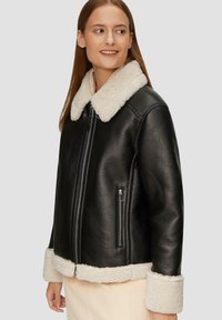 Czarna skórzana kurtka z kremowym kołnierzem i mankietami z owczej wełny. Posiada zamek błyskawiczny z przodu oraz boczne kieszenie na zamek, o prostokątnym kroju.