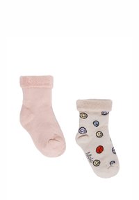 Różowa skarpeta z pluszowym mankietem obok kremowej skarpety z wesołym wzorem buźki. Obie charakteryzują się miękką teksturą i długością sięgającą kostki.