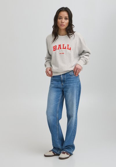 Pilkas džemperis su raudonu užrašu "BALL", derinamas su šviesiai mėlynomis tiesiomis kelnėmis ir smėlio spalvos sportiniais bateliais su burgundiškais akcentais.