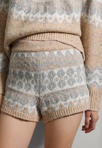 Pantalones cortos de lana con un patrón en beige, gris y blanco con diseños geométricos. Tejido texturizado con un acabado suave y cinturilla acanalada.