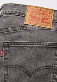 Jean en denim gris avec une coupe droite slim. Comprend une étiquette en cuir marron marquée "Levi Strauss & Co." et un onglet rouge sur le côté.
