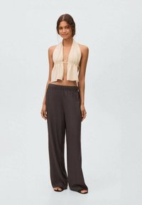 Beige halter top with flowy cut and a tie front, paired with loose, dark brown pants. Smooth textures and relaxed fit.