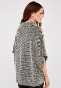 Top de gran tamaño en blanco y negro con textura, cuello de cisne y mangas cortas. Presenta un ajuste holgado y relajado, con aberturas laterales.