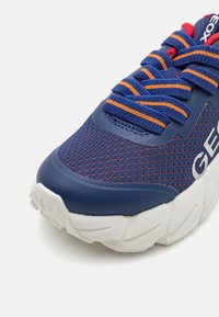 Blauwe sportieve schoen met een bovenwerk van mesh, oranje en blauwe veters, een gevoerde kraag en een witte, gestructureerde zool met uitgesproken groeven.