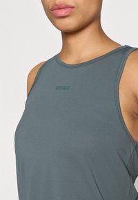 Bez piedurknēm pelēks topiņš, izgatavots no strukturētas auduma; tam ir apaļa kakla izgriezne un neliels "BORG" logo atbilstošā krāsā priekšā.