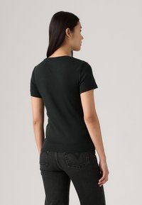 T-shirt noir ajusté à manches courtes et à encolure ronde. Tissu en coton lisse avec un design uni. Porté avec un jean foncé.
