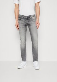 Grå smala jeans med en urtvättad design, med fem fickor och dragkedja. Kombinerat med vita sneakers och en enkel vit t-shirt.