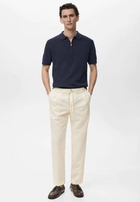 Camisa polo navy con cremallera y tejido texturizado, combinada con pantalones de lino beige claros y zapatos de cuero marrón oscuro con cordones.