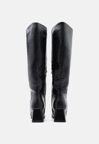 Bottes noires en cuir montantes jusqu'aux genoux avec un motif texturé crocodile, bouts carrés et talons épais. Finition lisse avec une fermeture éclair latérale.