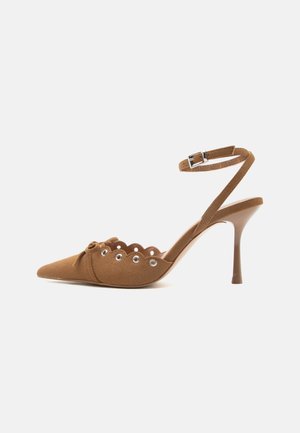 Brown suede high-heeled pump with pointed toe, scalloped edges, silver eyelet details, and ankle strap with buckle.