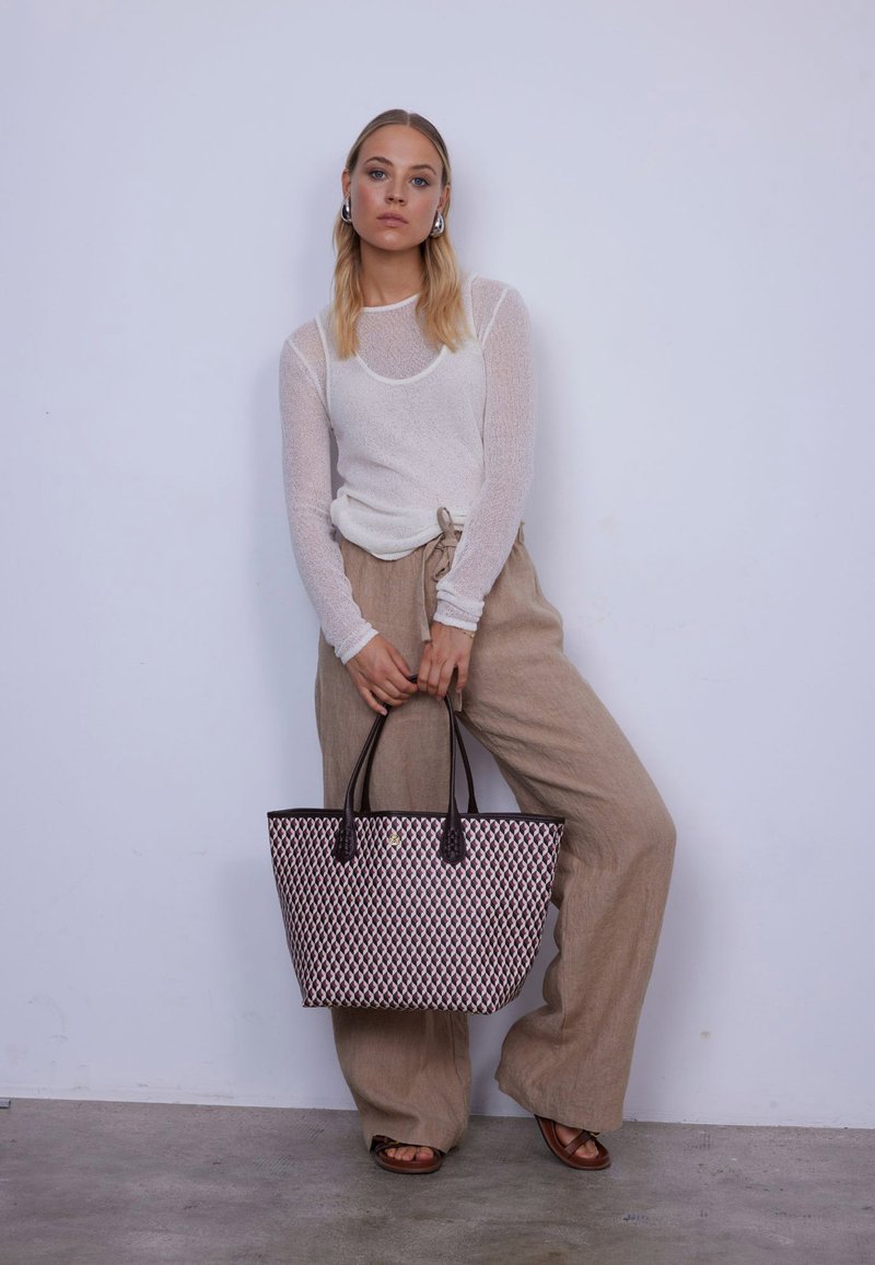 Geräumige Tragetasche im schwarz-cremefarbenen, gewebten Muster, mit braunen Ledergriffen und glatter Textur. Das Modell trägt lockere beige Hosen und ein Oberteil.