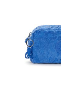 Sacchetto di tessuto blu con motivo floreale testurizzato, chiusura con zip e un charm a figura blu attaccato. Accento con logo rotondo sul lato.