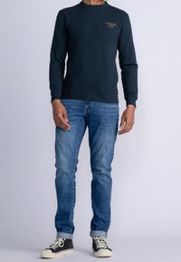 Sudadera azul marino con cuello redondo y puños acanalados, combinada con jeans de color azul claro y zapatillas altas negras con suelas blancas.