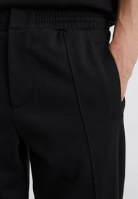 Black jogger pants made of soft fabric with an elastic waistband and side pockets, featuring a smooth texture and clean lines.
