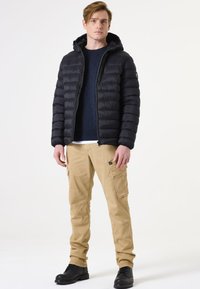 Zwarte pufferjack met een capuchon, ritssluiting en een boxy pasvorm; gecombineerd met beige cargobroek met zijzakken en een ontspannen pasvorm.