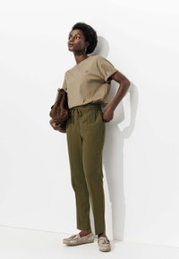 T-shirt beige avec détail en forme de cœur, pantalon vert olive avec taille élastique, et chaussures slip-on beiges. Les accessoires comprennent un sac imprimé léopard.