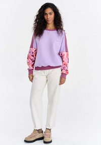 Lavendli toonides dressipluus lillemustriliste varrukatega, mida täiendab kreemjad püksid ja beežid matkasaapad. Varustatud ümmarguse kaelusega ja soonikkoes varrukaservadega.