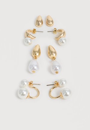 Quatre paires de boucles d'oreilles en or et perles disposées verticalement sur un fond blanc, chaque paire présentant des formes uniques et des accents de perles.