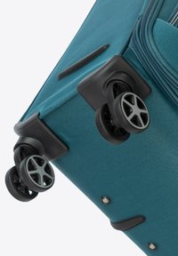 Turkusowa walizka na kółkach z teksturowaną powierzchnią, czterema czarnymi kołami, wzmocnionymi narożnikami oraz bocznym uchwytem dla łatwej manewrowalności.