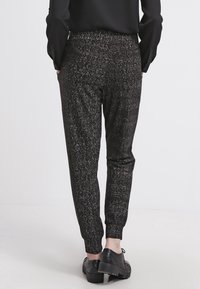 Czarne spodnie dresowe z taperowanym krojem i elastycznym paskiem, w zestawieniu z czarnymi butami na platformie. Teksturowany materiał ma subtelny wzór.