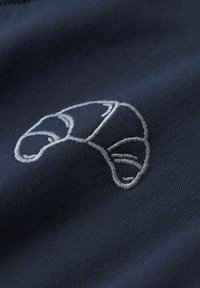 Le tissu bleu marine présente un motif de croissant gris brodé avec des détails texturés, mettant en valeur les formes courbes et les contours.
