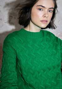 Groene trui met kabelmotief, gemaakt van een getextureerd garen. Voorzien van een ronde hals en een geribde zoom. Het breipatroon zorgt voor een golvend ontwerp door het hele kledingstuk.