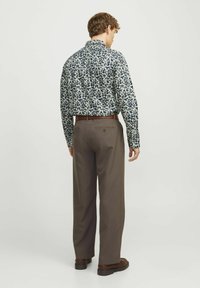 Chemise boutonnée bleu marine avec un motif floral blanc, associée à un pantalon marron. La chemise présente des manches longues et un design de col classique.
