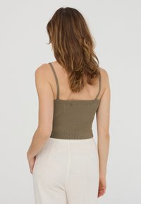 Top corto a coste verde oliva con spalline sottili, caratterizzato da un design aderente e un tessuto testurizzato, abbinato a pantaloni larghi di colore chiaro.