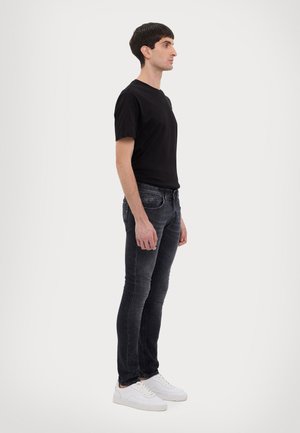 T-shirt nera a maniche corte abbinata a jeans slim-fit grigi scuri e sneakers bianche. L'outfit presenta un design semplice e moderno.