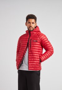 Giacca a vento rossa con imbottitura orizzontale, chiusura frontale con zip e cappuccio. Presenta una piccola tasca sul petto e polsini elasticizzati. Texture liscia.