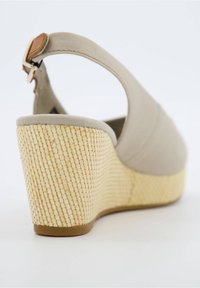 Sandale compensée beige avec talon à texture tissée, bride cheville et fermeture à boucle, vue depuis un angle bas arrière.