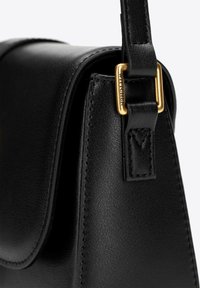 Černá kožená kabelka se strukturovaným tvarem, zdobená zlatými kovovými detaily a texturovaným povrchem. Součástí je odnímatelný popruh.