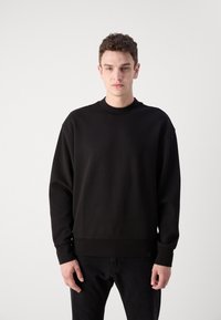 Felpa nera con girocollo, maniche lunghe e polsini a coste. Tessuto a contrasto all'orlo, realizzata in un morbido materiale.